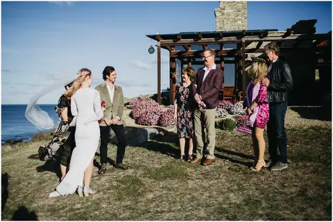 A couple walk past their wedding guests beside the ocean.